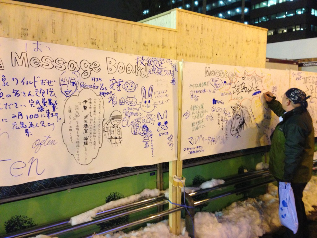 A passer by writes a message on a board set up in front of one of the festival structures. 