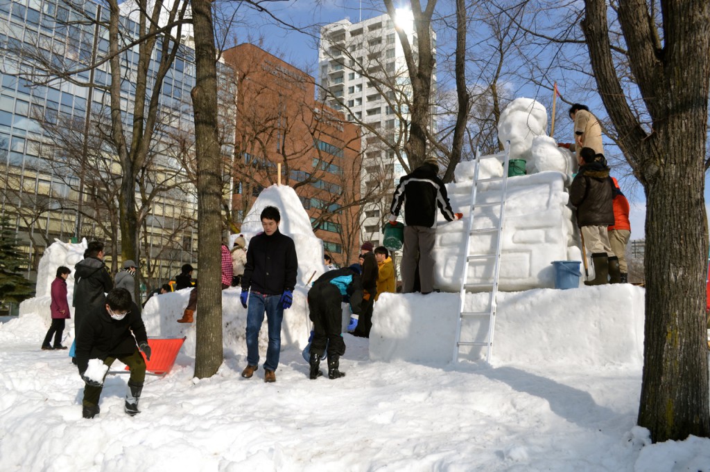 A group works on a sculpture, collecting snow from the nearby sidewalk to complete the job. 